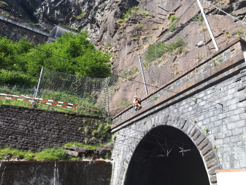 Rope-access technician inspecting rockfall protection nets above the Gotthard tunnel portal in Switzerland, supporting Impact Sentinel hazard monitoring.